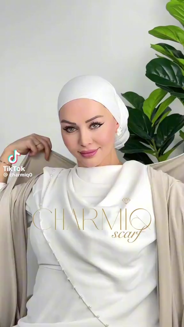 The image shows a woman wearing a white headscarf with gold accents, posing f… thumbnail